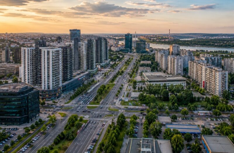 Panoramski pogled na Novi Beograd sa širokim bulevarima, modernim stambenim i poslovnim zgradama, zelenilom i rekom u pozadini