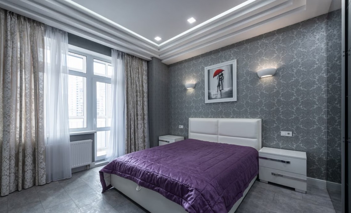 Spavaća soba sa plafonskom garnišnom, belom zavesom i sivim draperima uz veliki prozor